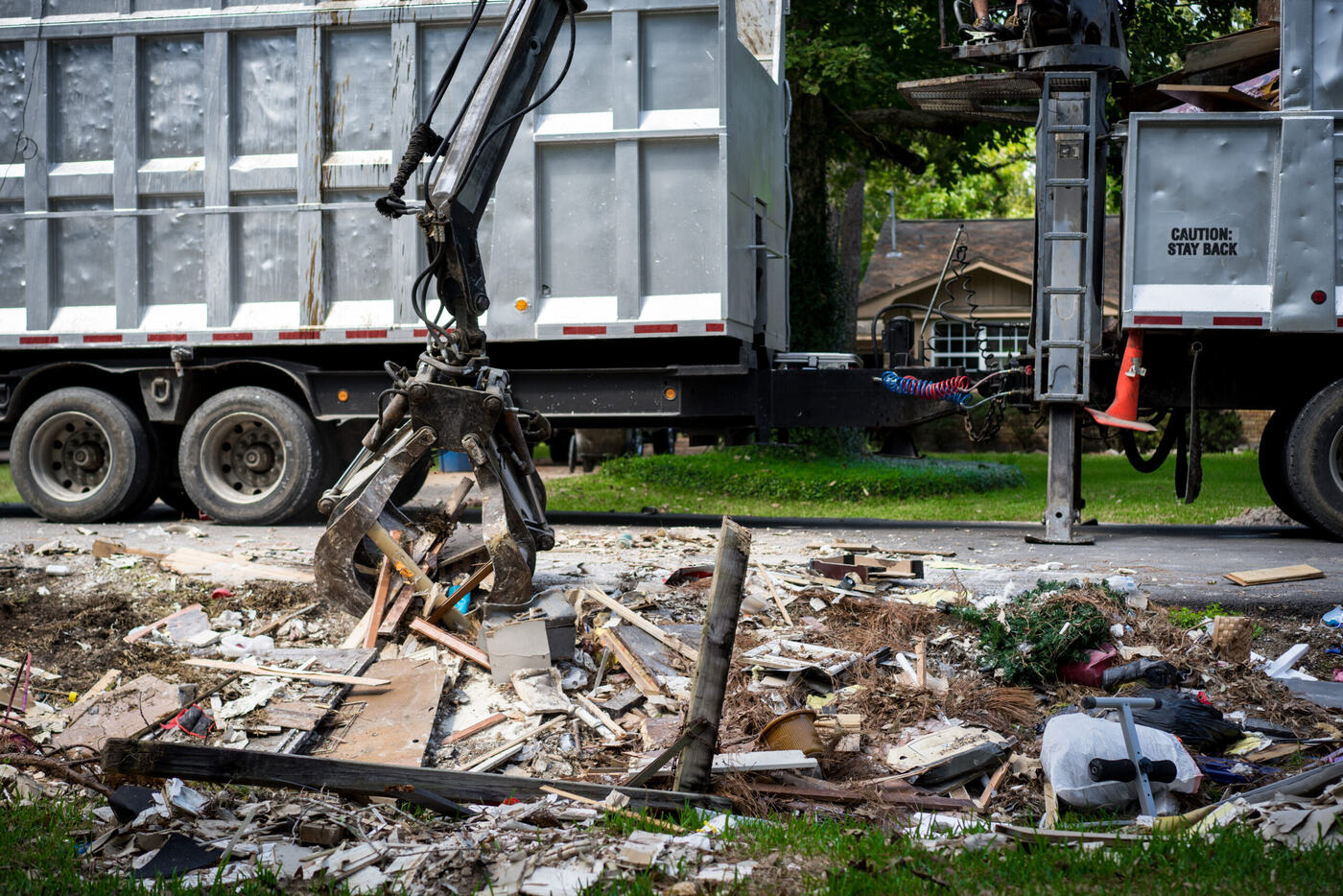 Grapple arm clearing mixed debris in front of a house